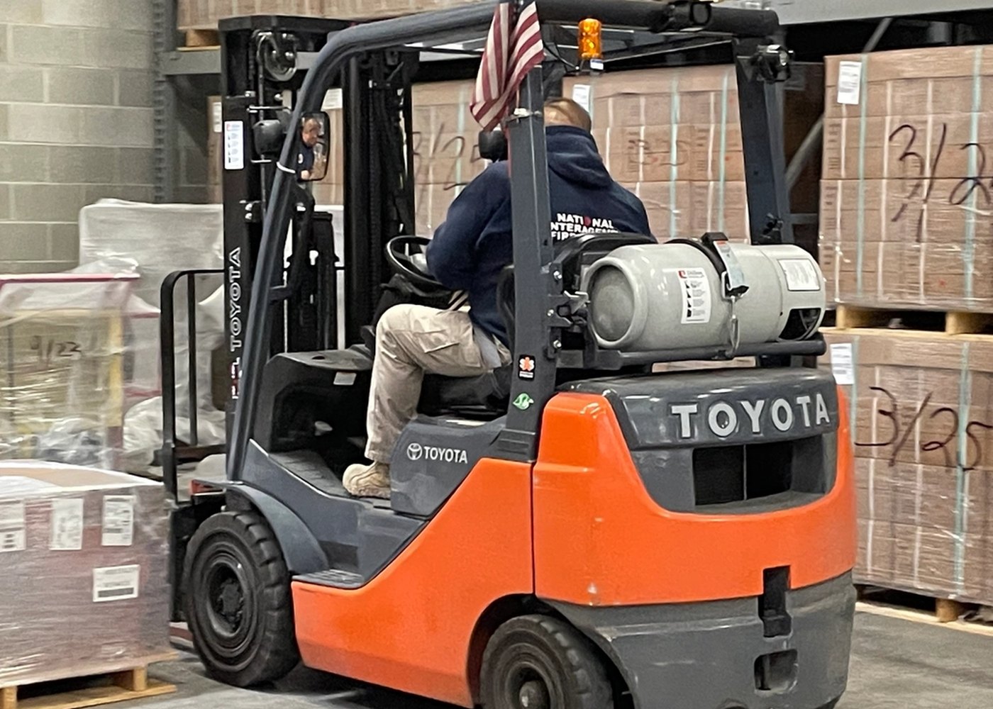 Operator driving an orange Toyota propane forklift past stacked pallets on a loading dock